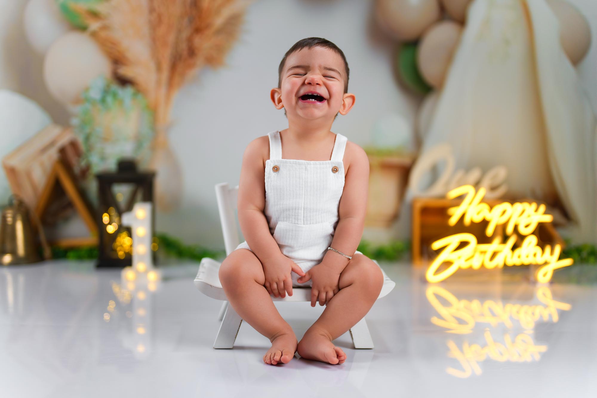 Ein Baby-Junge in einem weißen Outfit sitzt auf einem Hocker und hat einen emotionalen Moment während seines ersten Geburtstagsfotoshootings.