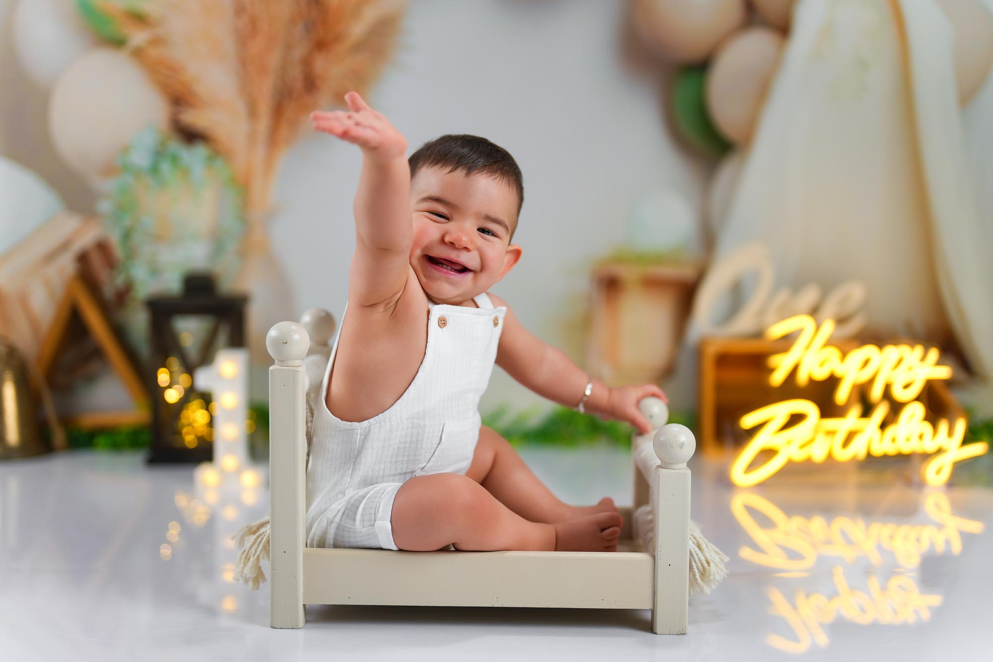 Ein fröhlicher Baby-Junge feiert seinen ersten Geburtstag und jubelt in seinem kleinen Bett vor einem Happy-Birthday-Schild.