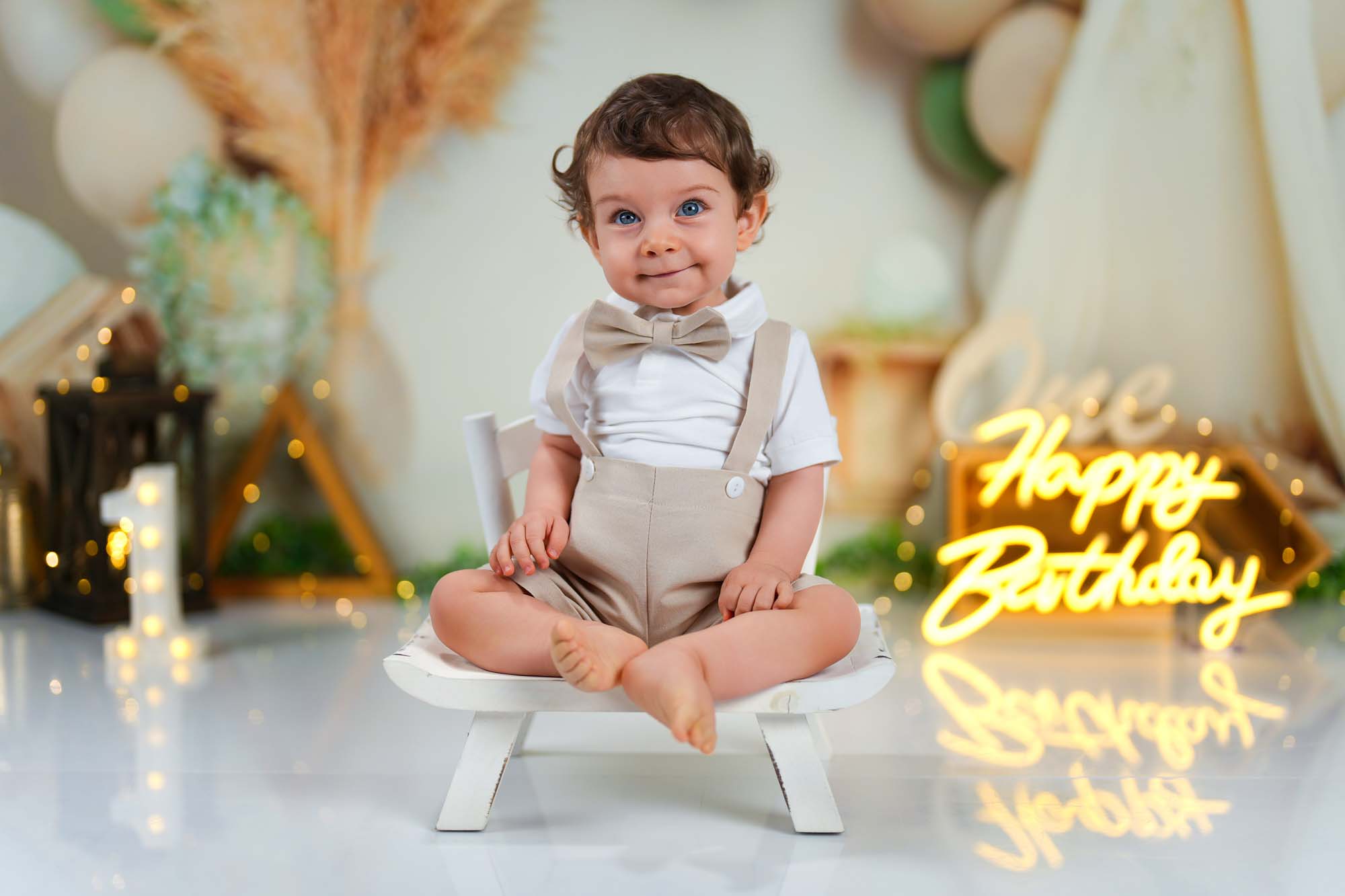 Kleiner Junge in festlicher Kleidung sitzt vor einem Neon-Happy-Birthday-Schild.