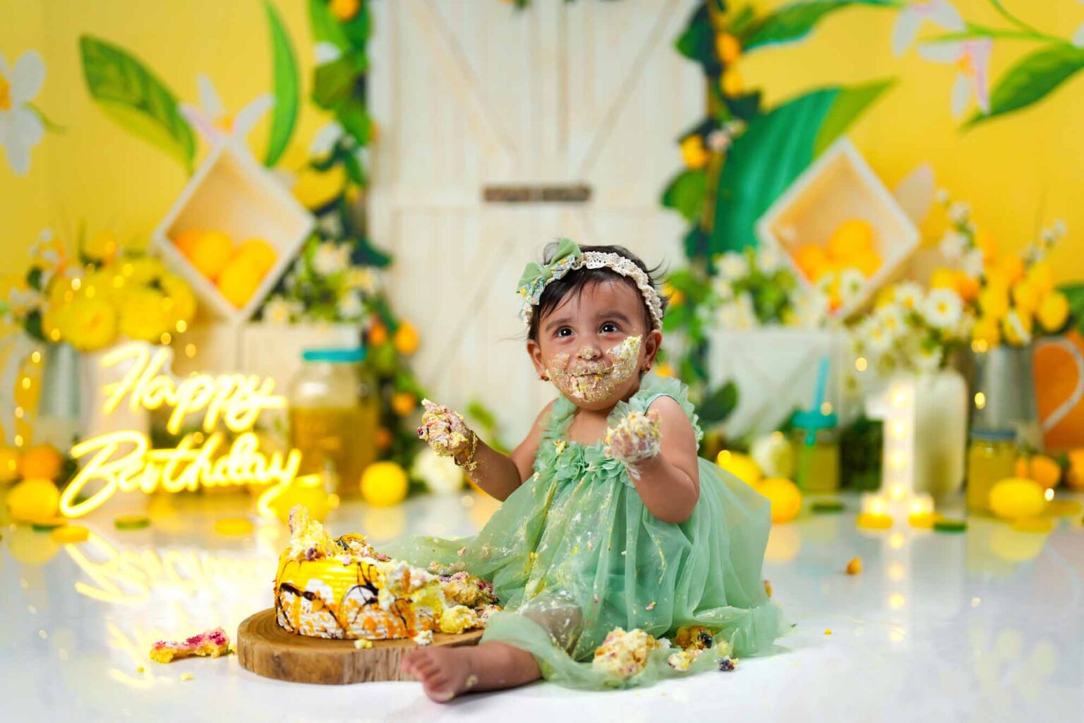 Ein fröhliches Cake-Smash-Shooting zum ersten Geburtstag, mit gelb-grüner Zitronen-Dekoration und lachendem Baby im grünen Kleid.