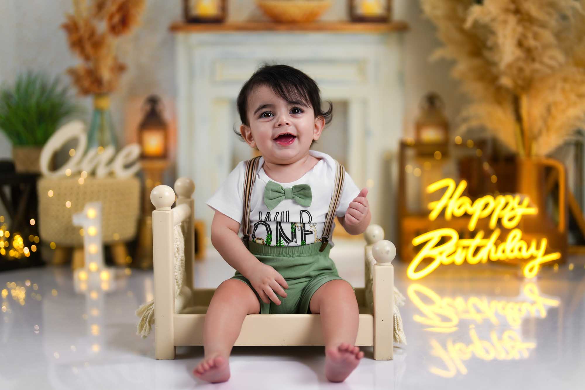 Ein kleiner Junge im „Wild One“-Outfit sitzt lachend auf einem Mini-Holzbett vor einer warm dekorierten Geburtstagskulisse.