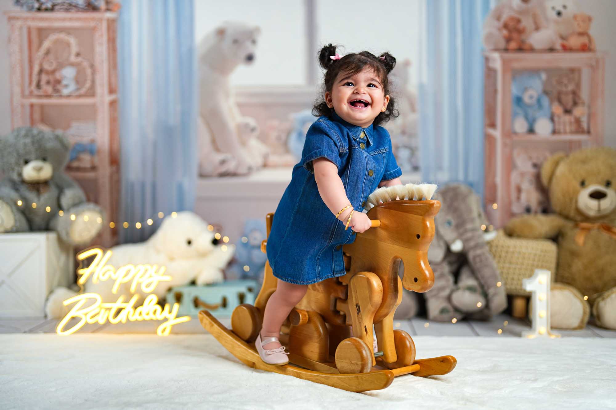 Lächelndes Mädchen auf einem Holzschaukelpferd beim 1. Geburtstagsshooting