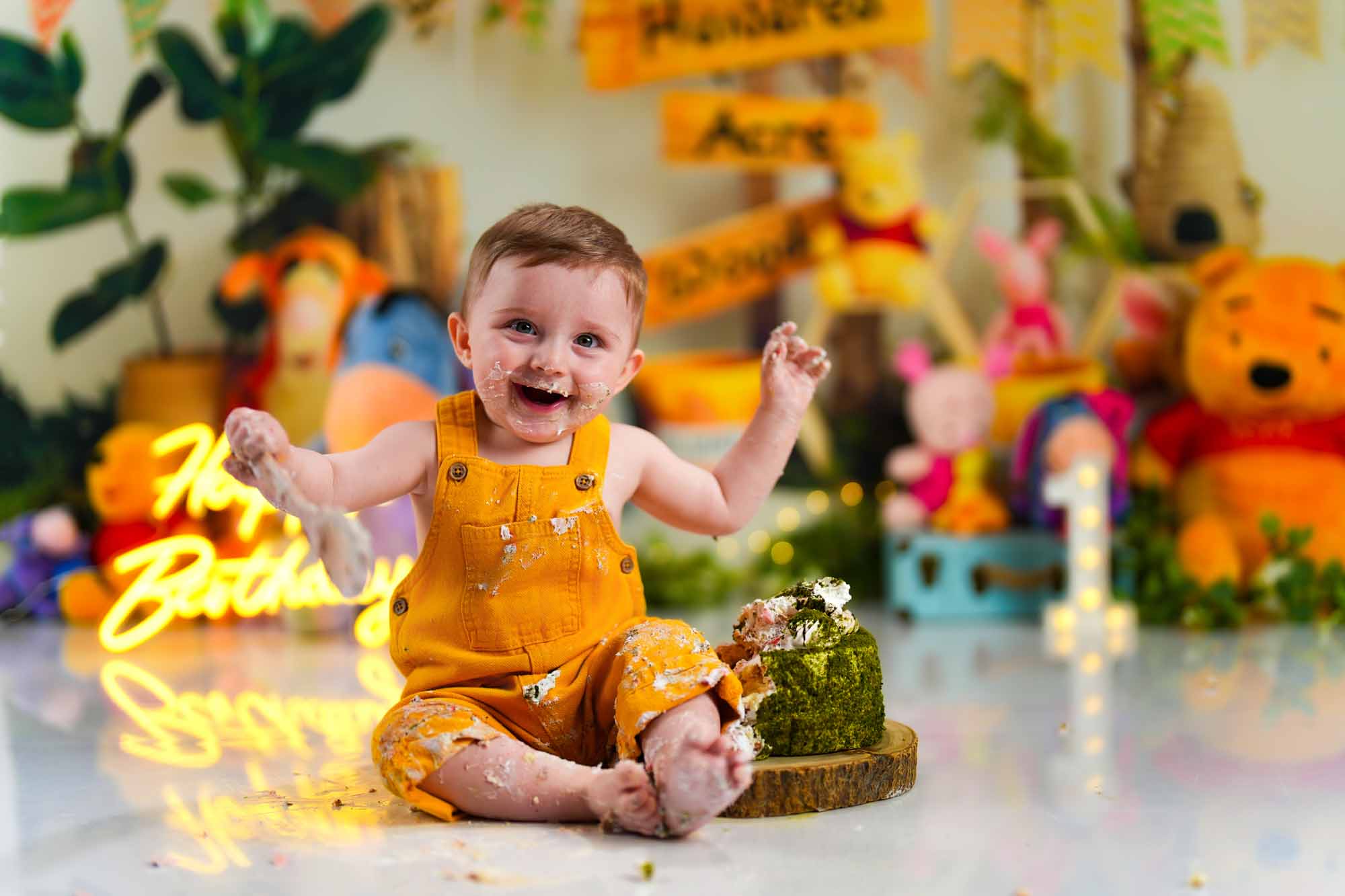 Baby im gelben Latzanzug beim Cake Smash Shooting mit Winnie the Pooh Dekoration.