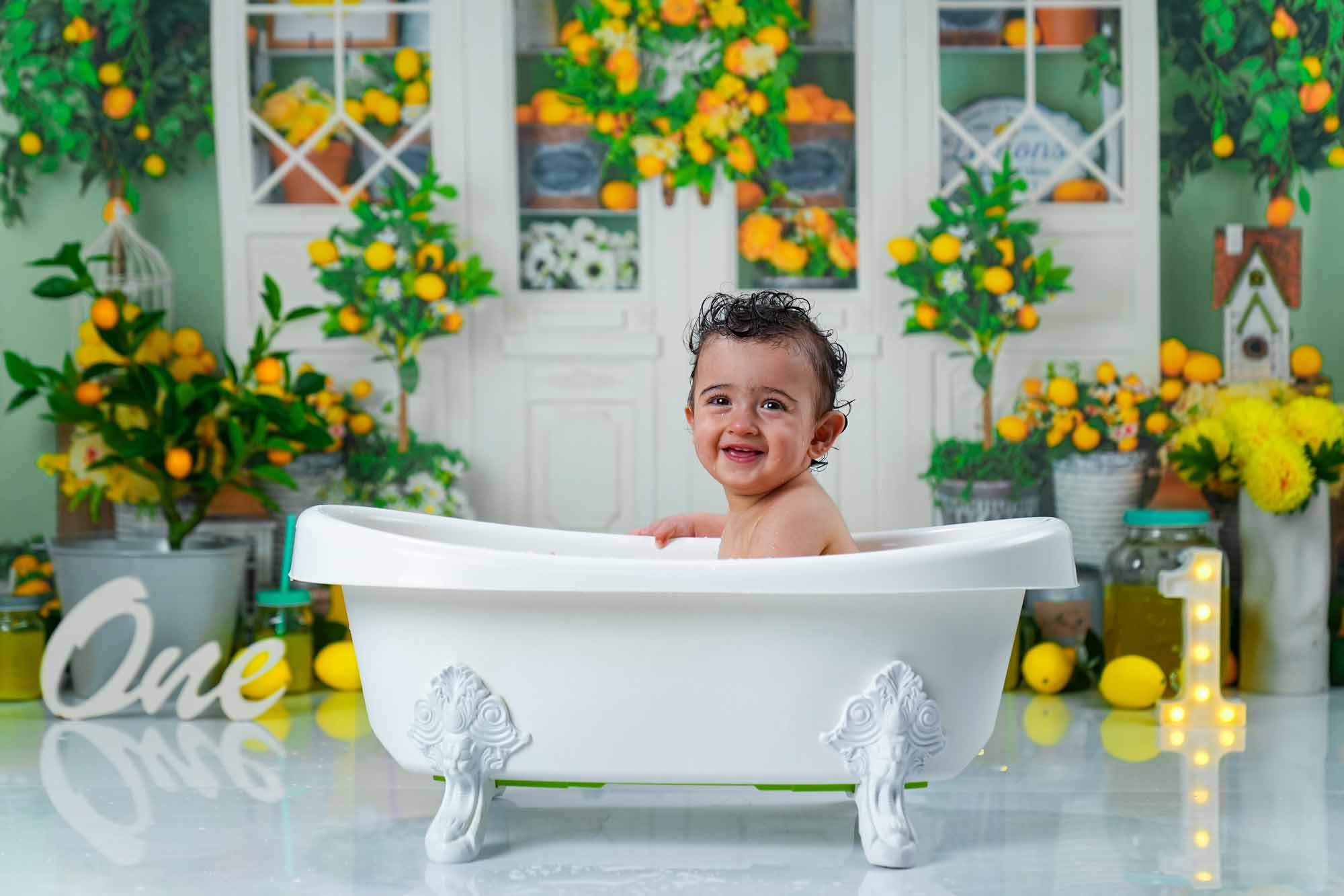 Lachendes Baby in einer weißen Vintage-Badewanne vor einem Zitronen-Backdrop.