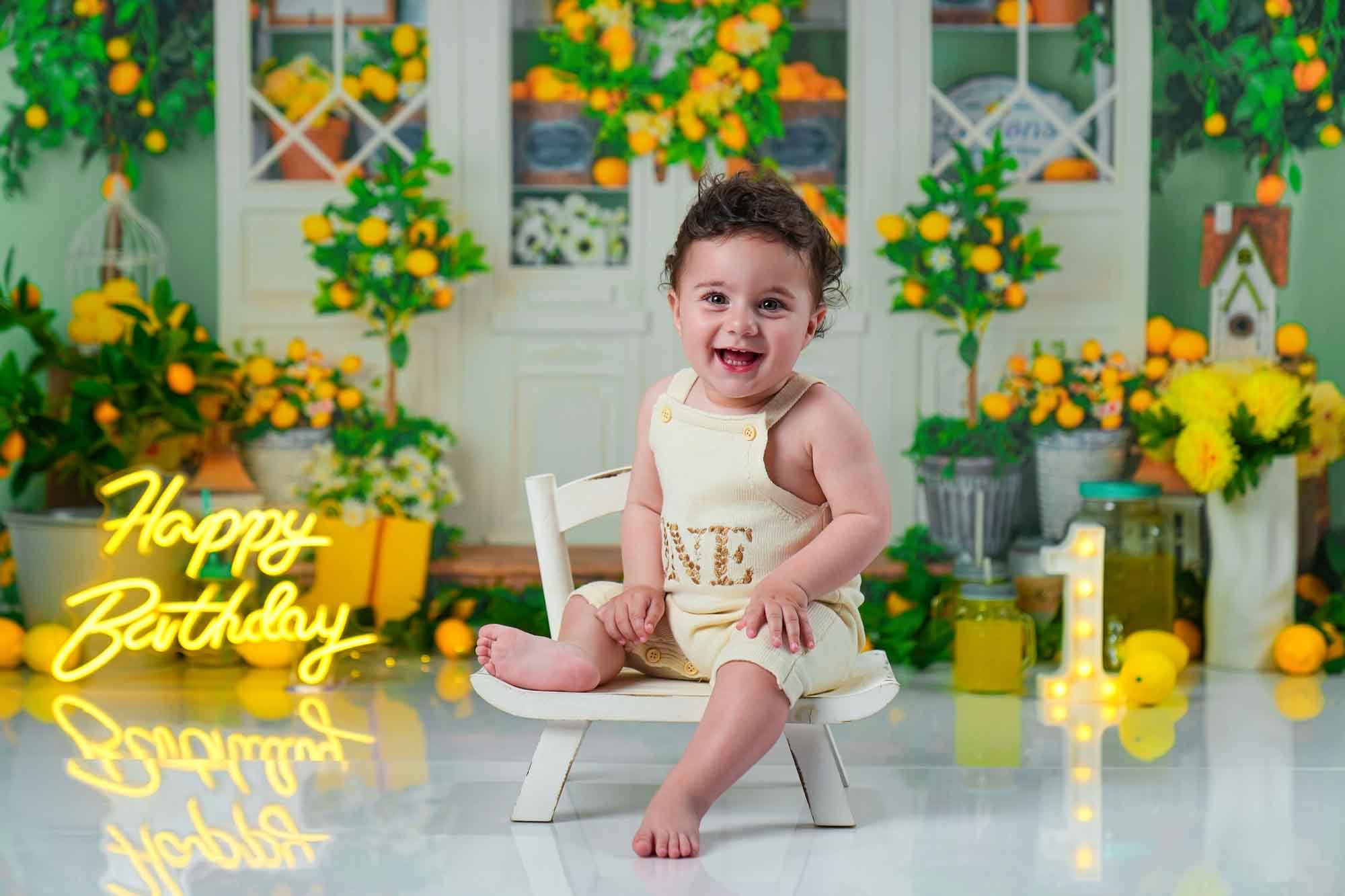 Baby im gelben Einteiler mit „One“-Schriftzug vor einem Zitronen-Hintergrund.