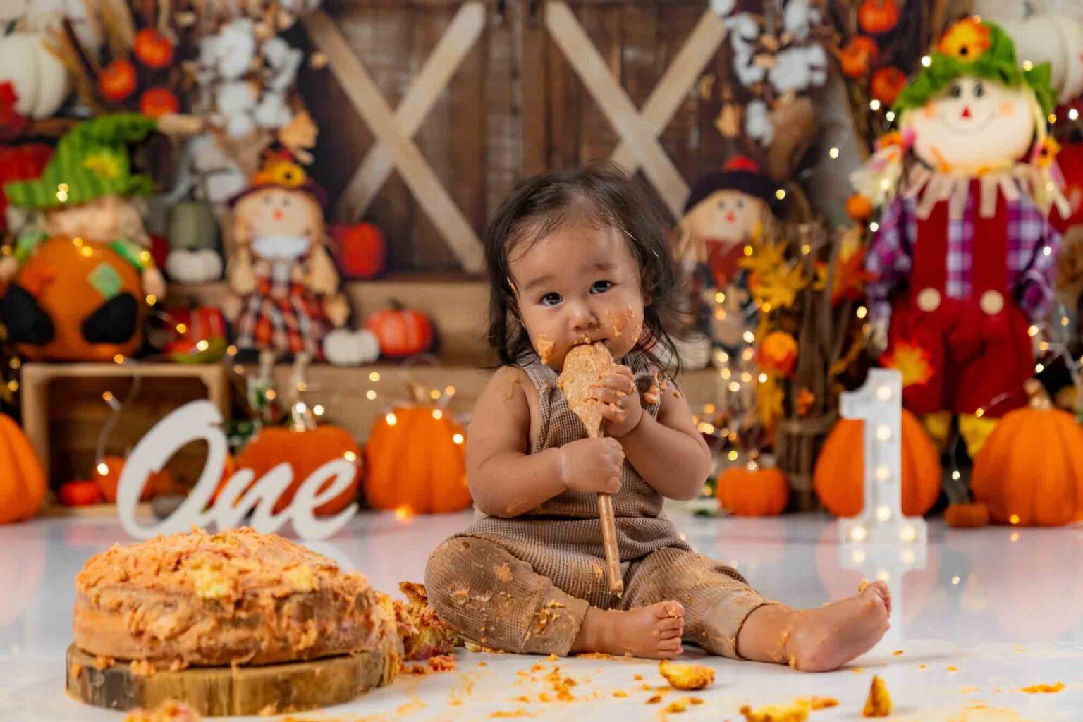 Ein Baby-Mädchen mit schmutzigem Gesicht isst ihre Geburtstagstorte während eines herbstlichen Cake-Smash-Shootings.