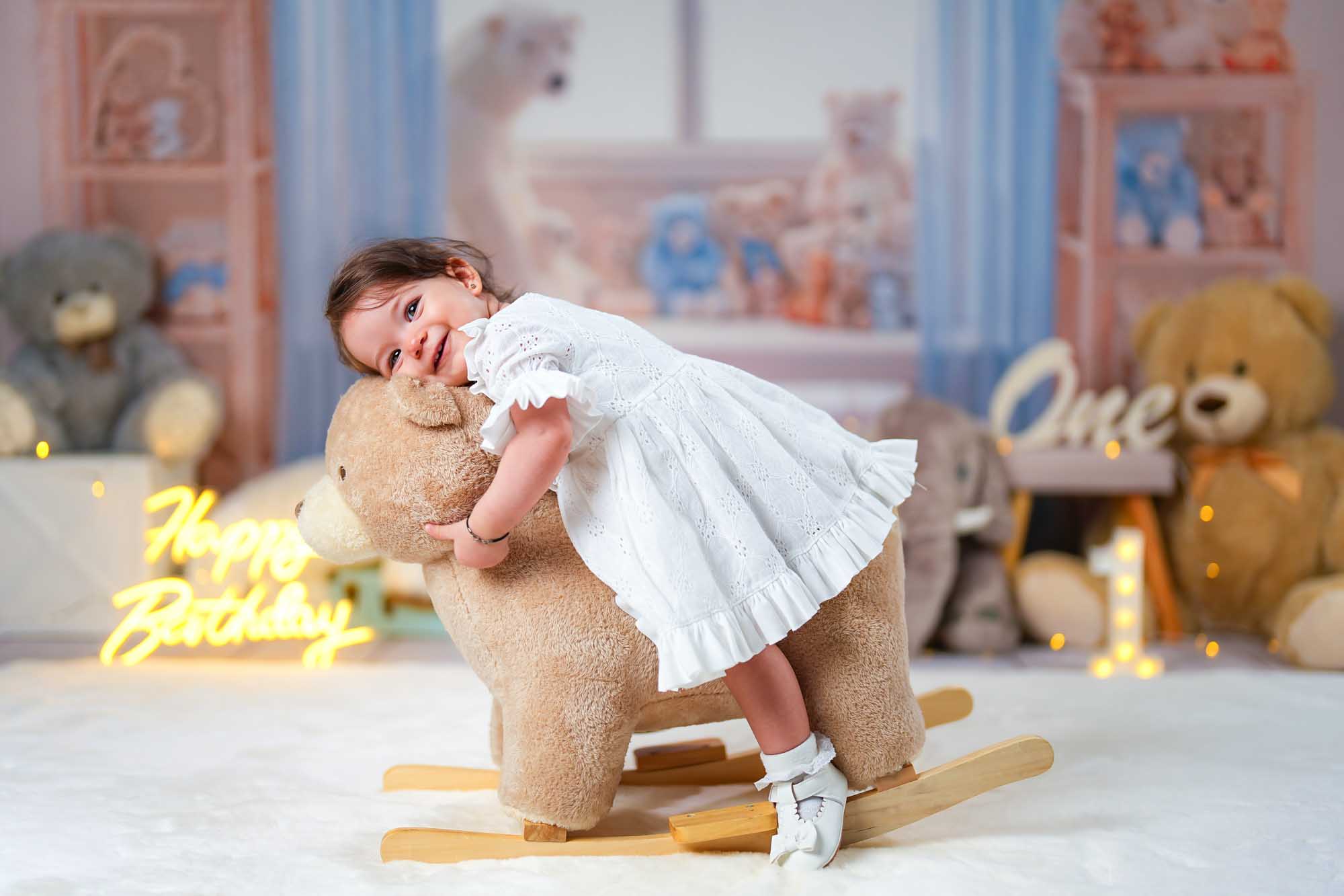 Mädchen im weißen Kleid reitet auf einem Plüsch-Schaukelpferd.