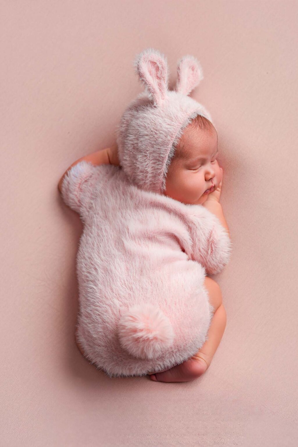 Neugeborenes im rosa Hasenkostüm, seitlich schlafend, Studio Wien